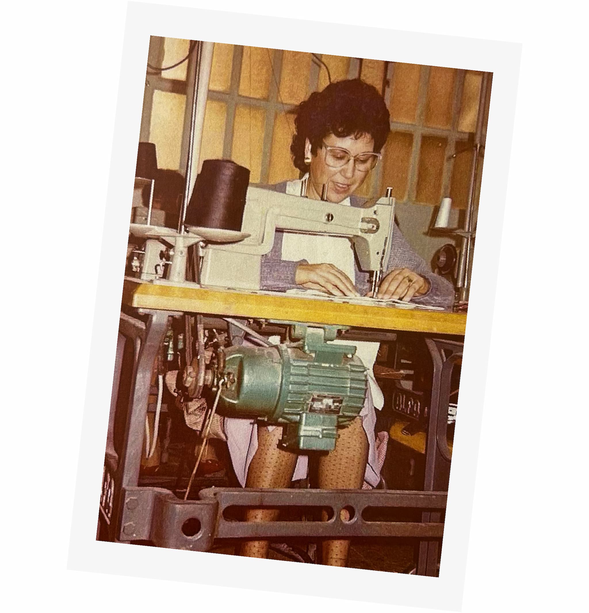 Fotografía vieja, con colores desgastados, de Lola Casademunt cosiendo a máquina, sentada, en su taller